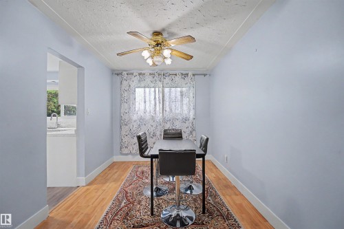 Dining area featuring wood-finish flooring, a ceiling fan with integrated lighting, and a window with sheer curtains - 12707 87 Street, Edmonton, AB 