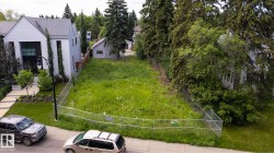 Expansive vacant lot featuring a grassy expanse, chain-link fencing, mature perimeter trees, and street frontage - 