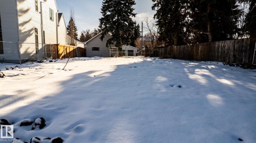 Expansive rear yard presenting a snow-covered lawn, mature perimeter trees, a wooden privacy fence, and a white vinyl-sided structure - 14307 Summit Drive, Edmonton, AB 
