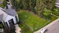 Expansive vacant lot featuring natural ground cover, partial chain-link fencing, mature perimeter trees, and street frontage - 