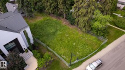 Expansive undeveloped lot with street frontage, featuring established perimeter trees and a chain-link fence - 