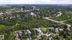 Urban landscape featuring extensive tree coverage, residential properties, a multi-lane roadway, and distant high-rise buildings - 