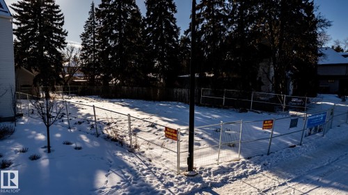Cleared lot featuring a temporary perimeter fence, a concrete sidewalk, and mature evergreen trees bordering the property - 14307 Summit Drive, Edmonton, AB 