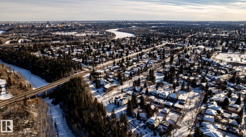 Aerial perspective showcasing a residential neighborhood with snow-covered rooftops, abundant mature trees, and a distant cityscape - 14307 Summit Drive, Edmonton, AB 