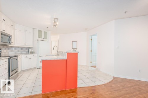 Kitchen featuring white cabinetry with silver hardware, stone countertops, and a white subway tile backsplash - 108 12028 103 Avenue, Edmonton, AB 