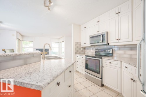 Kitchen featuring light-toned countertops, white cabinetry with dark hardware, a stainless steel electric range, and an over-the-range microwave - 108 12028 103 Avenue, Edmonton, AB 