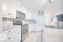 White kitchen featuring light-colored stone-finish countertops, stainless steel appliances, a subway tile backsplash, white cabinetry, and ceramic tile flooring - 108 12028 103 Avenue, Edmonton, AB 