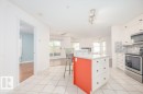 Spacious kitchen featuring white cabinetry, light-toned tiled flooring, stainless steel appliances, a center island with a granite-style countertop, and a subway tile backsplash - 108 12028 103 Avenue, Edmonton, AB 