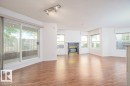 Spacious living area featuring wood-finish flooring, a decorative fireplace with a dark stone surround, and multiple windows providing ample natural light - 108 12028 103 Avenue, Edmonton, AB 