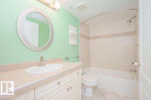 Bathroom featuring a single vanity with an integrated sink, brushed nickel faucet, and a large round mirror - 108 12028 103 Avenue, Edmonton, AB 