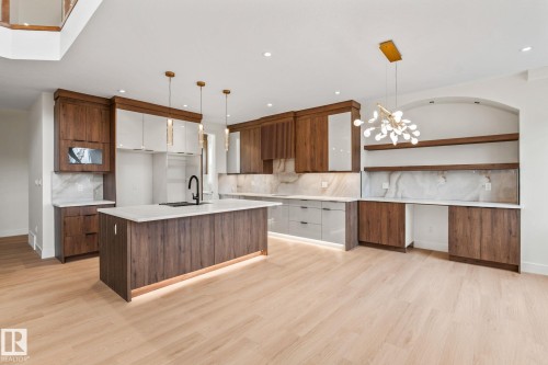 Gourmet kitchen with wood-finish and white cabinetry, a large kitchen island with under-cabinet lighting, light wood-finish flooring, and a contemporary chandelier - 13111 187 Avenue Nw, Edmonton, AB - Indoor Photo Showing Kitchen With Upgraded Kitchen