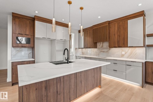 Contemporary kitchen featuring a large central island with a solid surface countertop, warm wood-finish cabinetry, sleek light gray lower cabinets, and integrated backsplash lighting - 13111 187 Avenue Nw, Edmonton, AB - Indoor Photo Showing Kitchen With Upgraded Kitchen