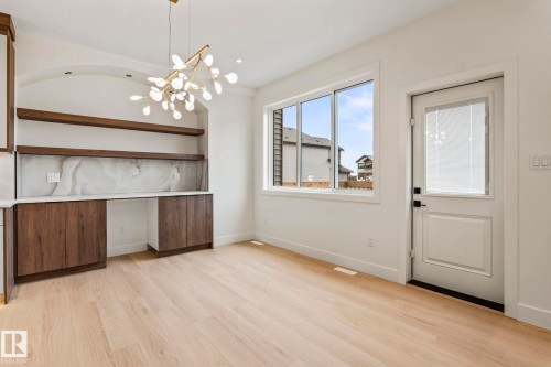 Built-in cabinetry with wood-finish doors and open shelving, large window with white trim, light wood-finish flooring, white paneled door with integrated blinds, and a contemporary light fixture - 13111 187 Avenue Nw, Edmonton, AB - Indoor Photo Showing Other Room