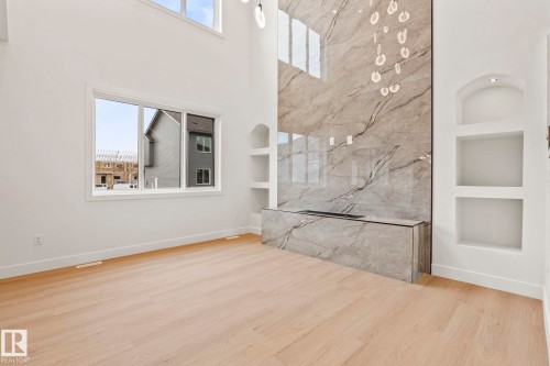 High ceilings with upper windows, light wood-finish flooring, full-height stone-clad accent wall, integrated linear fireplace, and recessed display niches - 13111 187 Avenue Nw, Edmonton, AB - Indoor Photo Showing Other Room
