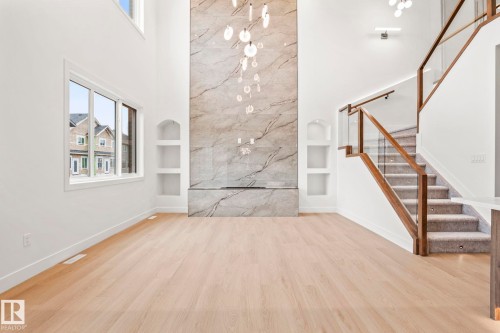 Double-height ceiling, wood-finish flooring, custom built-in shelving, glass and wood-frame staircase, and a floor-to-ceiling stone-look fireplace - 13111 187 Avenue Nw, Edmonton, AB - Indoor Photo Showing Other Room