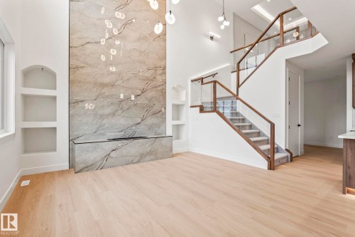 High ceilings with recessed lighting, light wood-finish flooring, built-in shelving, a full-height stone-finish accent wall with a built-in linear fireplace, and a multi-level staircase featuring glass railings and a wood-finish handrail - 13111 187 Avenue Nw, Edmonton, AB - Indoor Photo Showing Other Room