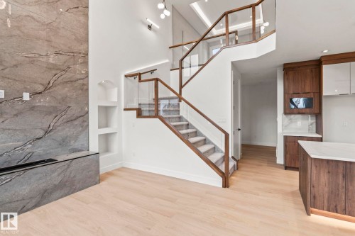 Grand staircase with glass railings and wood accents, light wood-finish flooring, built-in shelving, stone-finish fireplace surround, and kitchen cabinetry with light countertops - 13111 187 Avenue Nw, Edmonton, AB - Indoor
