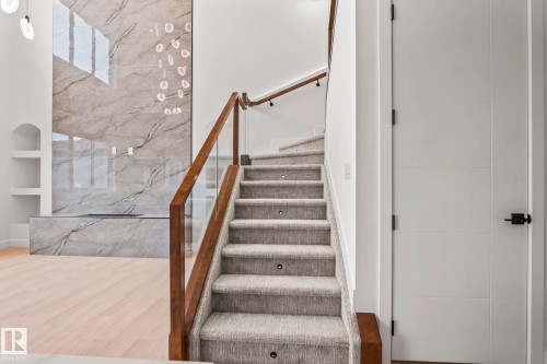 Carpeted staircase with integrated lighting and glass railing, wood-finish flooring, and a stone-clad fireplace with built-in shelving - 13111 187 Avenue Nw, Edmonton, AB - Indoor Photo Showing Other Room