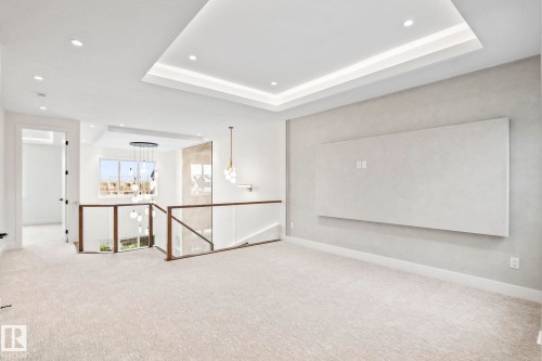 Recessed ceiling lighting, tray ceiling with accent lighting, wall-mounted display panel, glass railing with wood-finish top, and a contemporary chandelier - 13111 187 Avenue Nw, Edmonton, AB - Indoor Photo Showing Other Room
