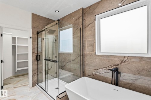 Freestanding soaking tub with a floor-mounted matte black faucet, glass-enclosed shower with a rain showerhead, built-in shelving, and large format wall and floor tiling - 13111 187 Avenue Nw, Edmonton, AB - Indoor Photo Showing Bathroom