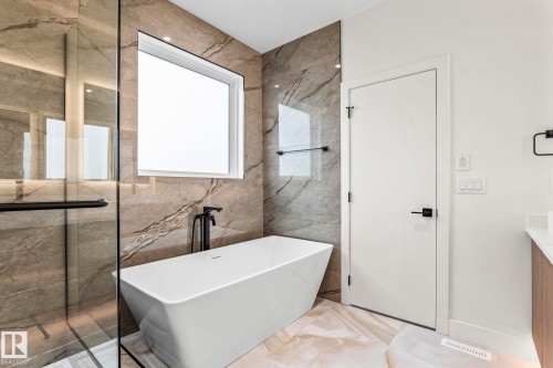 Freestanding soaking tub with a matte black floor-mounted faucet, large format stone tile walls, and a glass-enclosed shower - 13111 187 Avenue Nw, Edmonton, AB - Indoor Photo Showing Bathroom