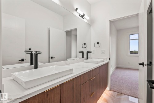 Dual vessel sinks with matte black faucets, a full-width vanity mirror, a stone countertop, and wood-finish cabinetry with gold-tone hardware - 13111 187 Avenue Nw, Edmonton, AB - Indoor Photo Showing Bathroom