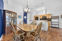 Open-concept dining area featuring wood-finish flooring, a contemporary chandelier, and a kitchen pass-through with pendant lighting - 