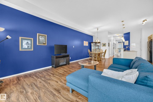 Open-concept living space featuring wood-finish flooring throughout, a distinctive accent wall, recessed lighting, and a built-in media console with an electric fireplace - 410 10531 117 Street, Edmonton, AB 