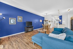 Open-concept living space featuring wood-finish flooring throughout, a distinctive accent wall, recessed lighting, and a built-in media console with an electric fireplace - 