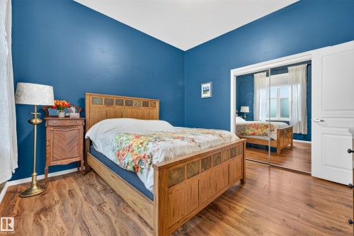 Bedroom featuring wood-finish flooring, a mirrored closet, and a white six-panel door - 410 10531 117 Street, Edmonton, AB 