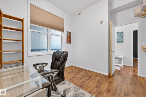 Room featuring wood-finish flooring, white walls, and a large window with privacy glass - 410 10531 117 Street, Edmonton, AB 