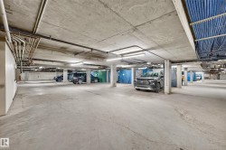 Spacious concrete parking garage with multiple support columns, exposed overhead piping, and integrated fluorescent lighting - 