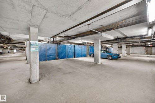 Spacious concrete parking garage with exposed ceiling infrastructure, multiple support pillars, and integrated lighting fixtures - 410 10531 117 Street, Edmonton, AB 
