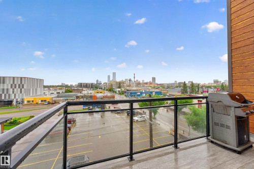 Expansive outdoor balcony featuring a glass and metal railing, wood-look siding, and a cityscape backdrop - 410 10531 117 Street, Edmonton, AB 