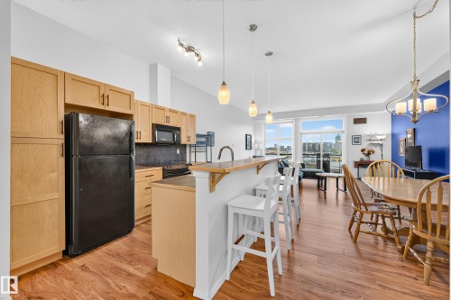 Open-concept living space featuring wood-finish flooring, a kitchen island with breakfast bar seating, recessed lighting, and large windows - 410 10531 117 Street, Edmonton, AB 