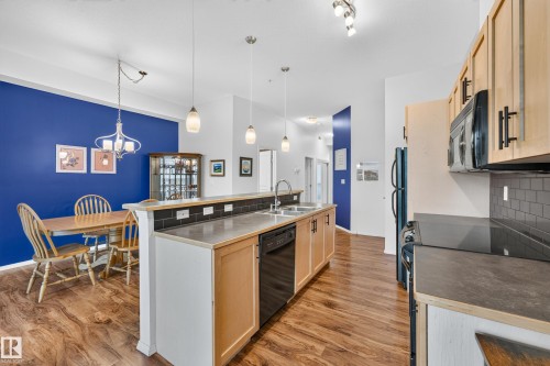 Kitchen and dining area featuring wood-finish flooring, light wood cabinetry, black appliances, a black subway tile backsplash, and a peninsula with integrated sink and seating - 410 10531 117 Street, Edmonton, AB 
