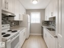 Galley kitchen featuring white cabinetry, light wood-finish flooring, mosaic tile backsplash, and light-toned countertops - 6348 180St, Edmonton, AB 