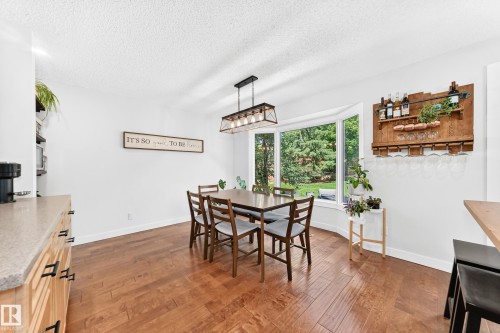 Dining space featuring wood-finish flooring, a prominent bay window, and a modern linear chandelier - 15146 Ramsay Crescent, Edmonton, AB 