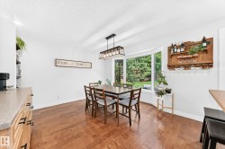 Dining space featuring wood-finish flooring, a prominent bay window, and a modern linear chandelier - 