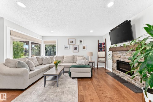 Living area featuring wood-finish flooring, a stone-faced fireplace with a wood mantel, recessed ceiling lighting, and large windows - 15146 Ramsay Crescent, Edmonton, AB 