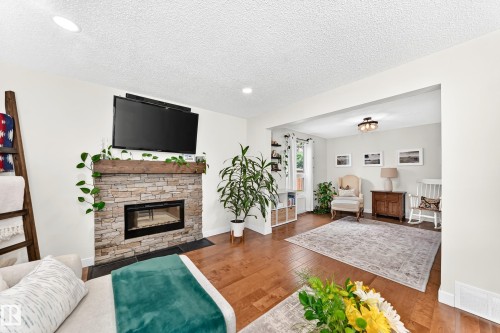 Stacked stone fireplace with a rustic wood mantel, complemented by recessed lighting and wood-finish flooring - 15146 Ramsay Crescent, Edmonton, AB 