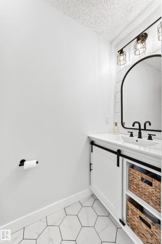 Bathroom vanity featuring a white countertop with integrated sink, black dual-handle faucet, and an arched black-framed mirror - 15146 Ramsay Crescent, Edmonton, AB 