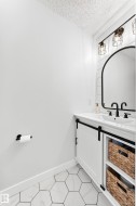 Bathroom vanity featuring a white countertop with integrated sink, black dual-handle faucet, and an arched black-framed mirror - 