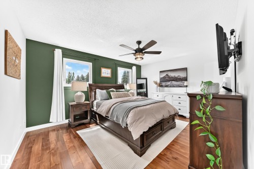 Bedroom featuring rich wood-finish flooring, a contemporary ceiling fan, and multiple windows - 15146 Ramsay Crescent, Edmonton, AB 