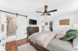 Bedroom with wood-finish flooring, a ceiling fan, and a white barn door - 