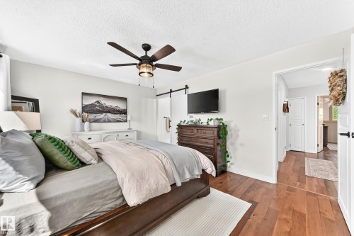 Bedroom featuring wood-finish flooring, a ceiling fan with integrated lighting, and a white barn door - 15146 Ramsay Crescent, Edmonton, AB 