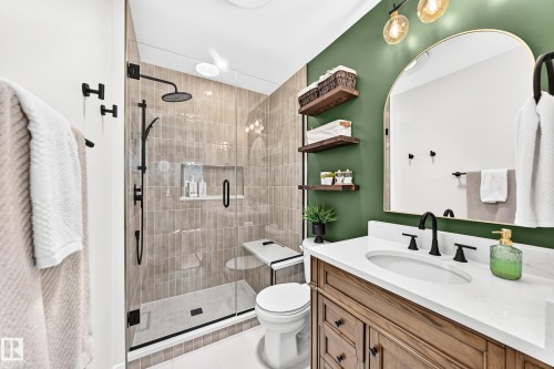 Bathroom featuring a glass-enclosed shower with vertical tile surround and built-in niche, a rainfall showerhead, and a wall-mounted shower wand - 15146 Ramsay Crescent, Edmonton, AB 