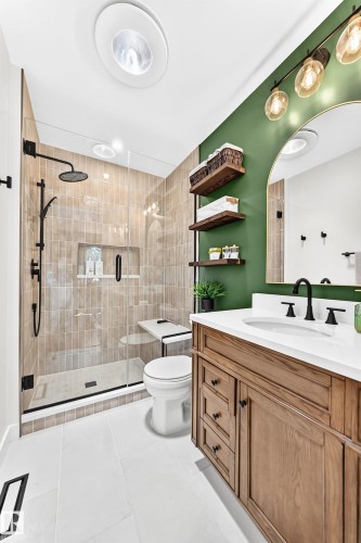 Modern bathroom featuring a glass-enclosed shower with tile surround and bench, a wood-finish vanity with a white countertop and undermount sink, matte black fixtures, and recessed ceiling lighting - 15146 Ramsay Crescent, Edmonton, AB 