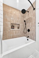 White bathtub with matte black fixtures, set against a tiled shower surround - 