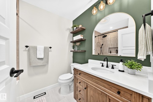 Bathroom featuring a wood-finish vanity with a white countertop, an arched mirror, and a three-bulb vanity light fixture - 15146 Ramsay Crescent, Edmonton, AB 